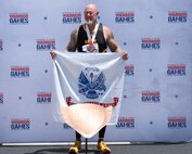U.S. Army veteran Steve Bortle poses for a photo with his medal and the Army flag at the track during the 2024 Department of Defense Warrior Games