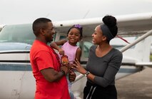 Man, and family smile as they pose next to airplane.