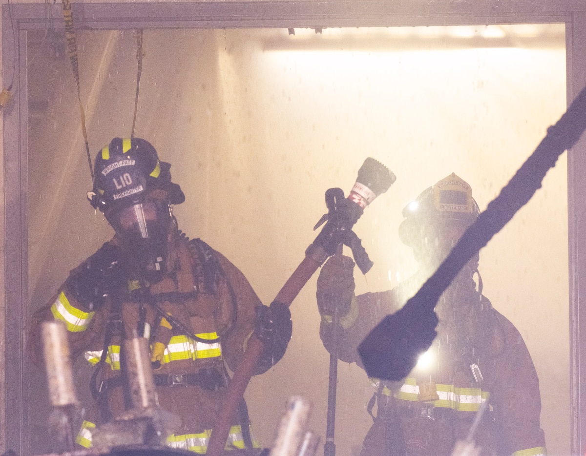 Two firefighters handle a hose in a smoky space