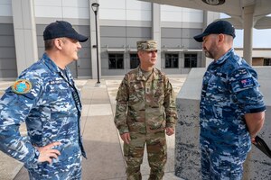 Three men in military uniforms talk.