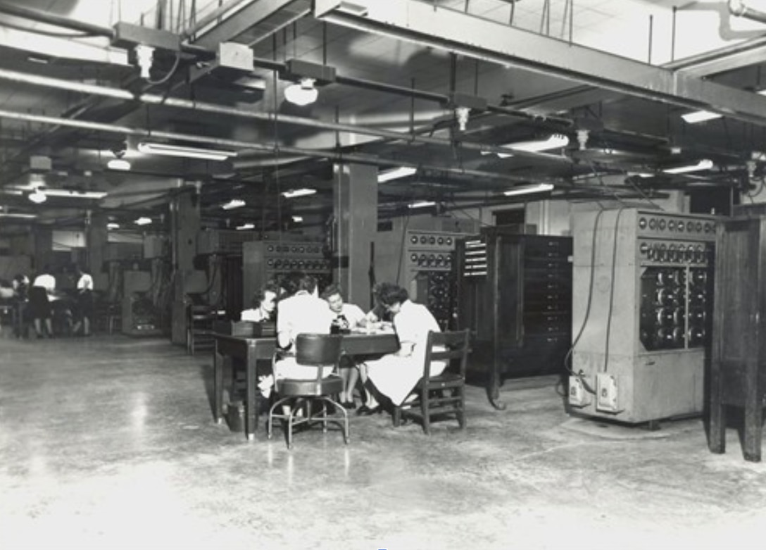 WAVES work alongside U.S. Navy Bombe machines at the main deck of Building No. 4 of OP-20-G’s Naval Communication Annex on Nebraska Avenue in Washington, DC, on 25 May 1945. There were 26 N-530s Bombes on this main deck.