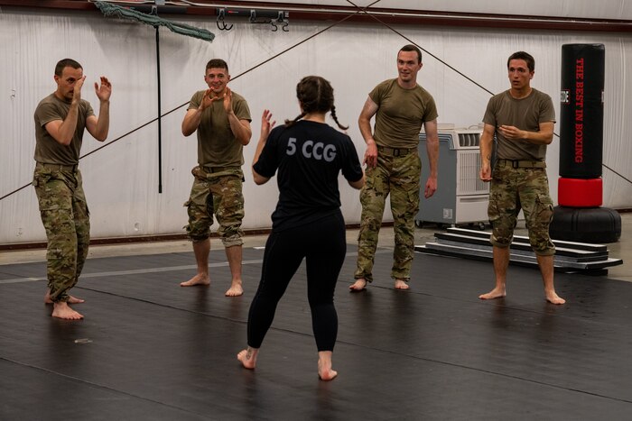 Airmen circle an instructor and receive combatives training