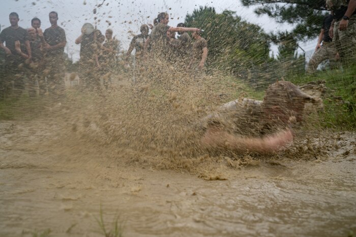 An Airman leaps into a mud pit