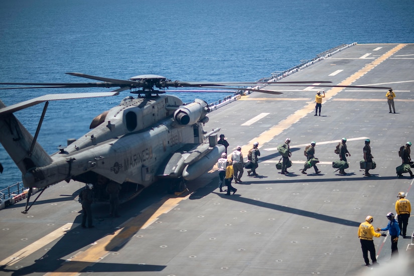 Marines walk away in a line from a helicopter parked on the flight deck of a ship at sea.