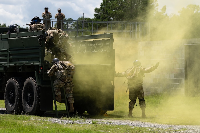 A group of Airmen evacuate a truck as a yellow smoke grenade goes off