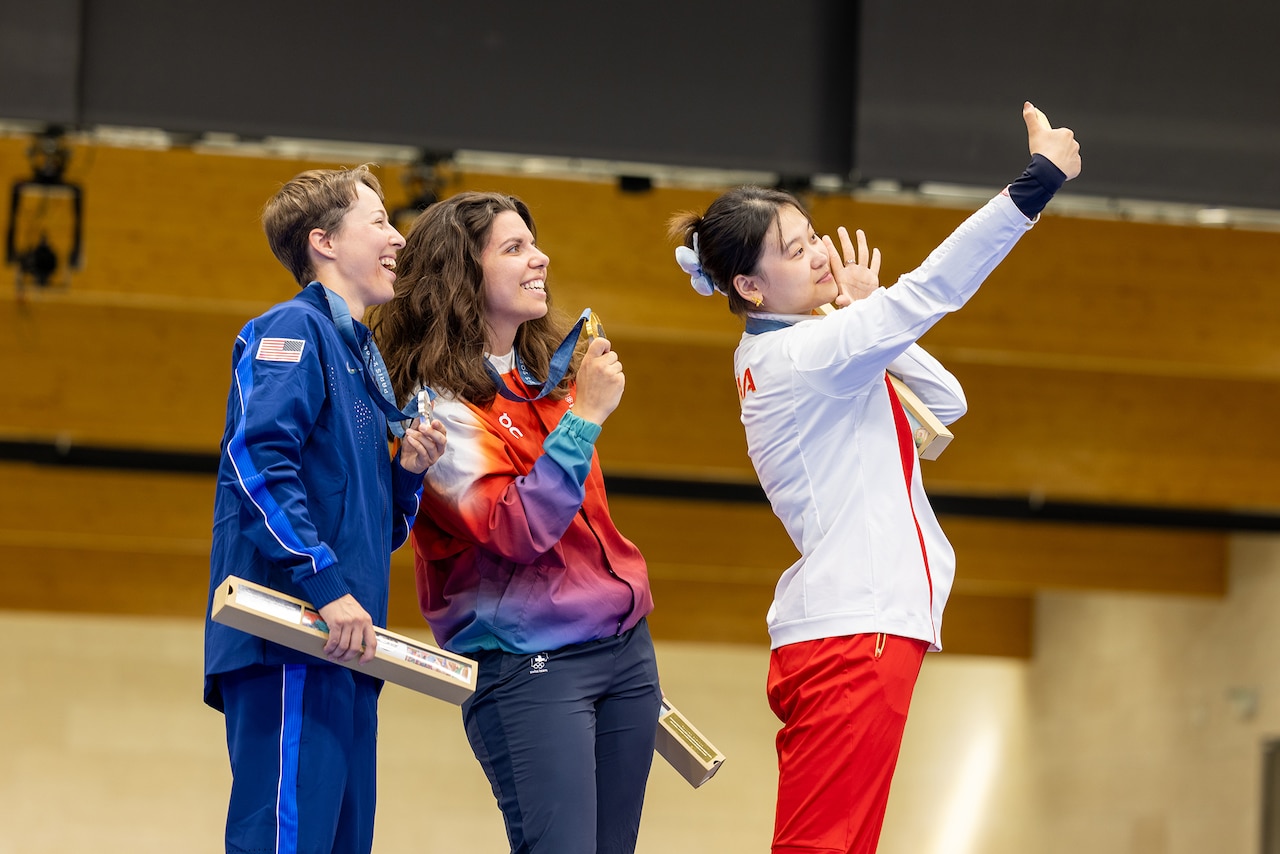 Three people stand on a podium and pose for a cell phone selfie.