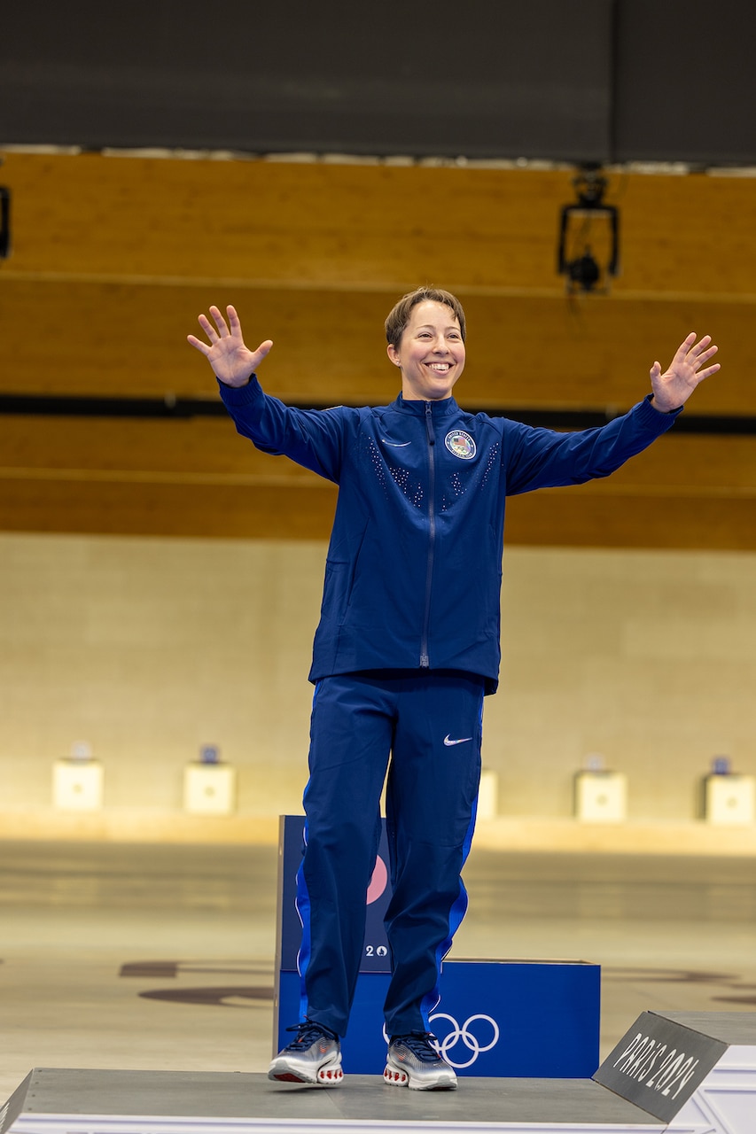 A soldier in athletic wear stands on a podium with their hands in the air.