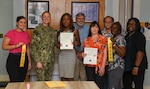 NMRTC Camp Lejeune Commanding Officer CAPT Anja Dabelić and members of the Health Promotion and Wellness team display the 2023 and 2022 Navy Surgeon General's Health Promotion and Wellness “Blue H” Award at a ceremony.