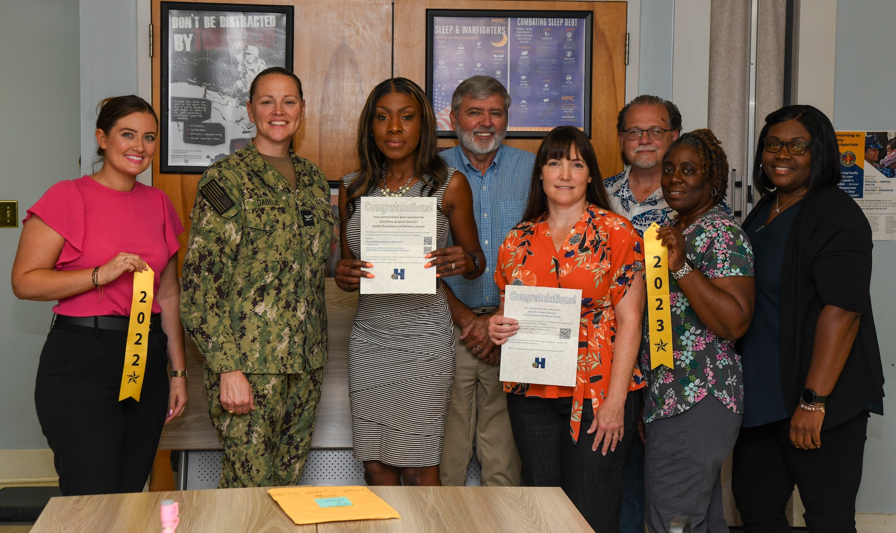 NMRTC Camp Lejeune Commanding Officer CAPT Anja Dabelić and members of the Health Promotion and Wellness team display the 2023 and 2022 Navy Surgeon General's Health Promotion and Wellness “Blue H” Award at a ceremony.