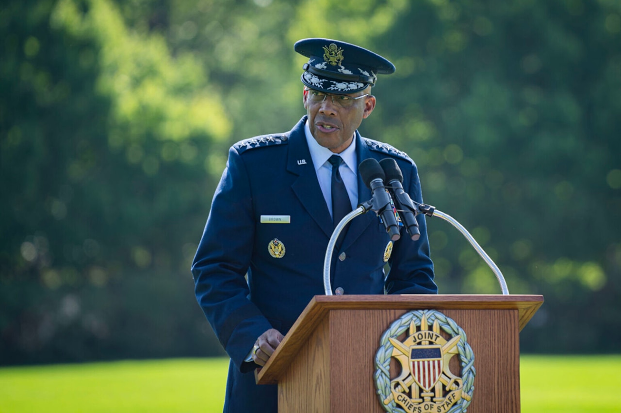 A person in military dress speaks from a podium outdoors.