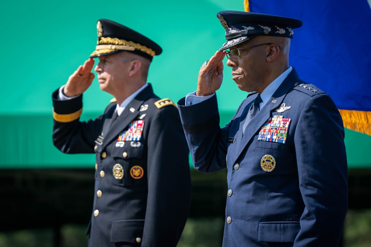 Two people in military uniforms salute.