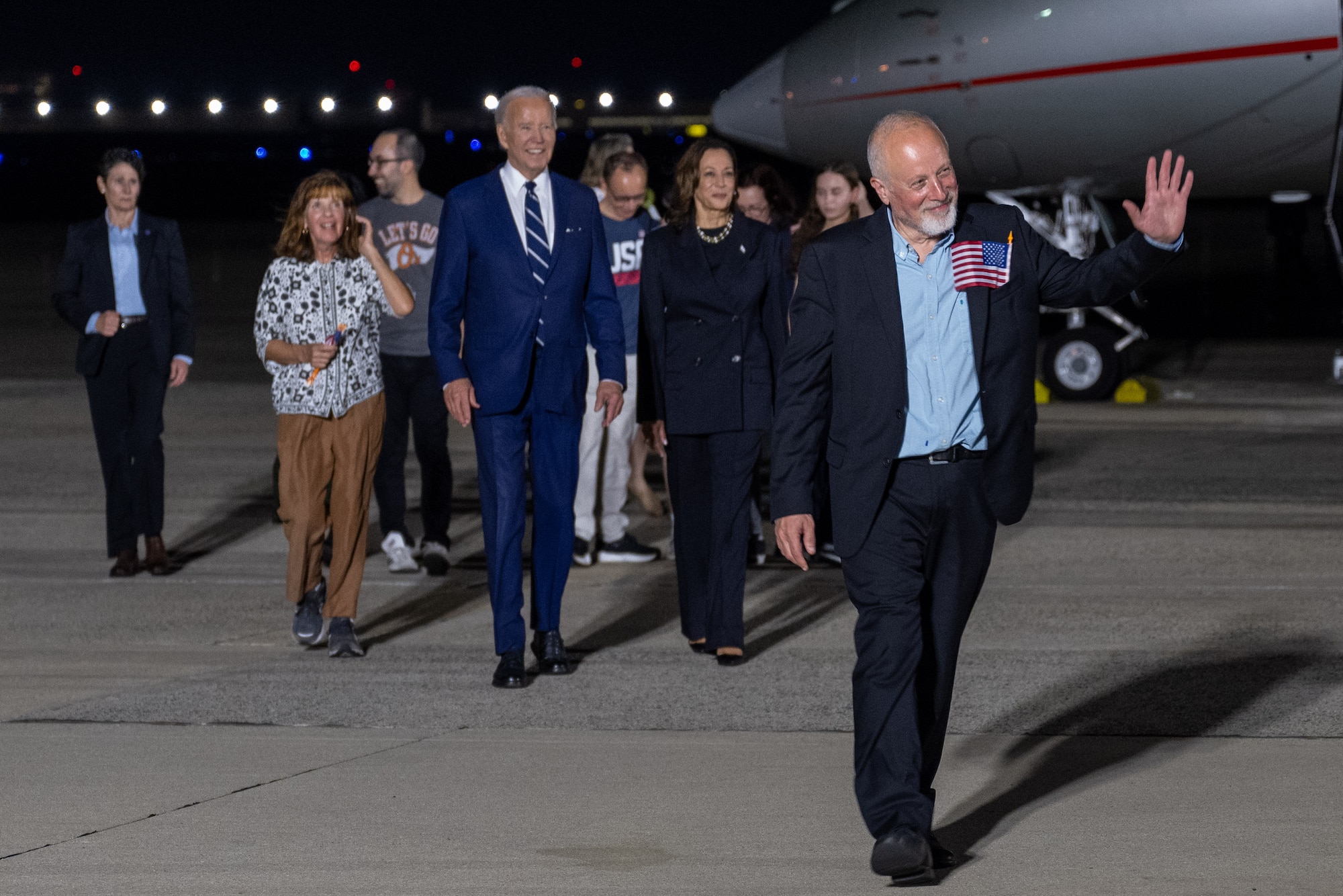 A crowd of people walk in front of a plane.