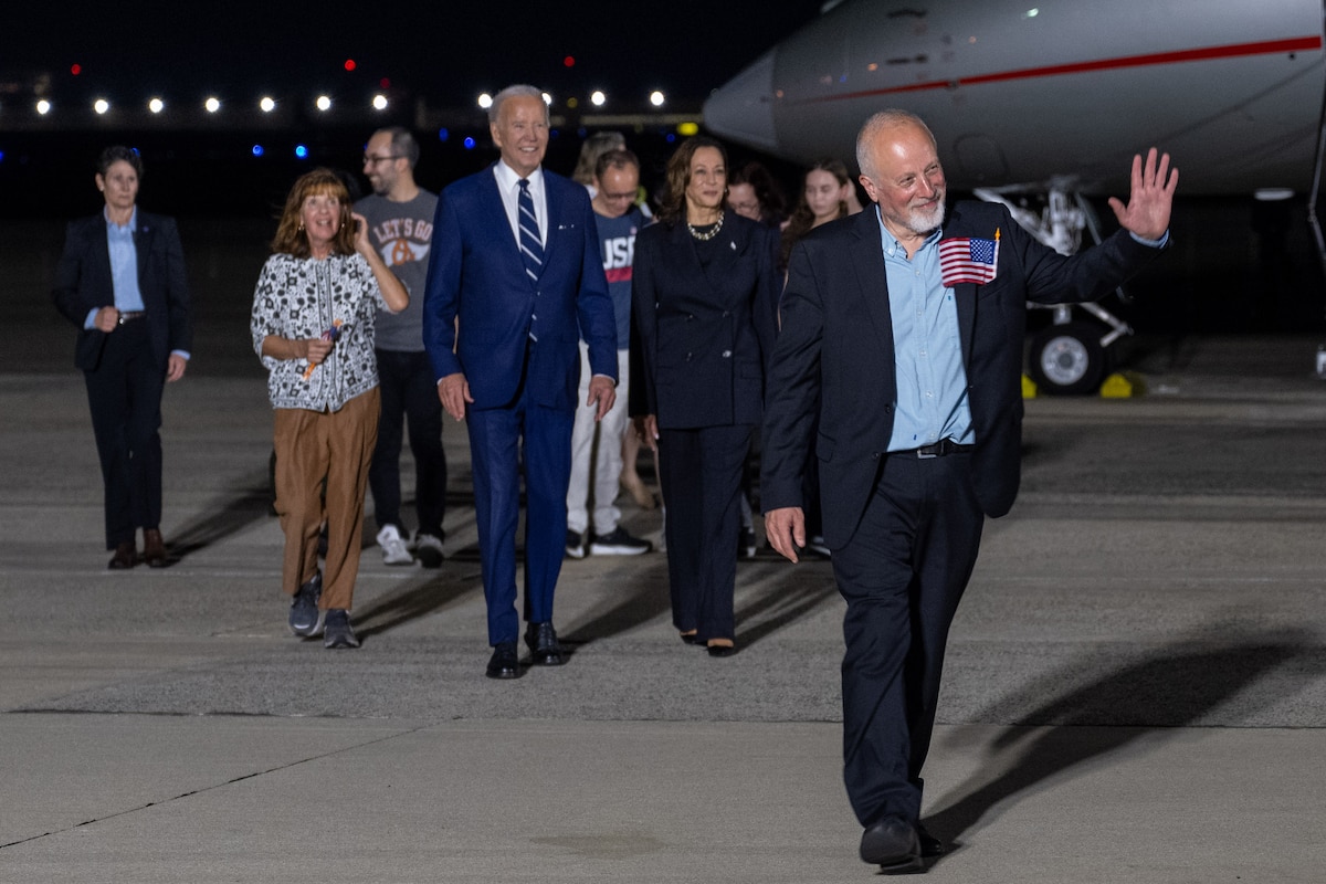 A crowd of people walk in front of a plane.