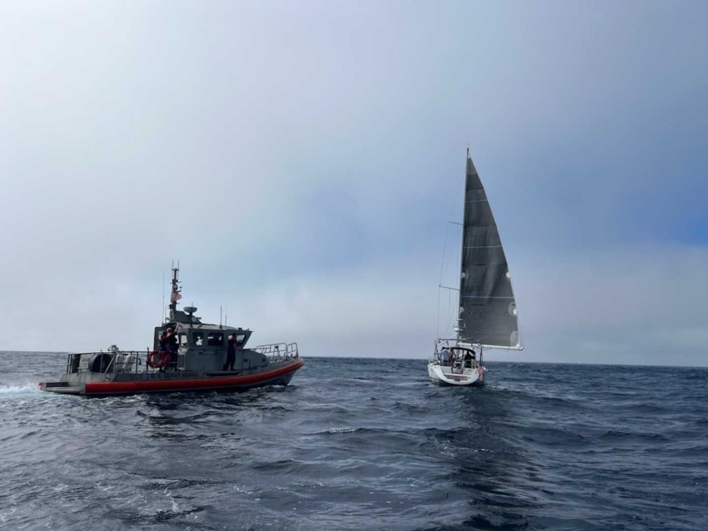 A Coast Guard 45-foot Response-Boat Medium approaches a sailboat in the ocean.