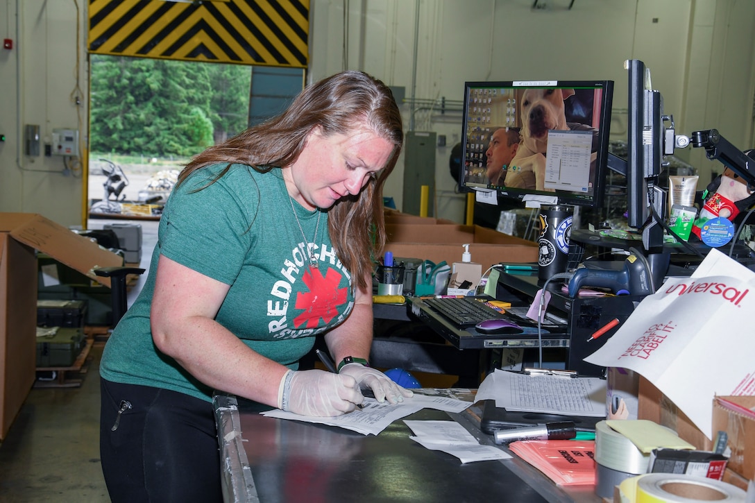 Woman in green shirt stands at a workstation doing paperwork while wearing a green shirt.