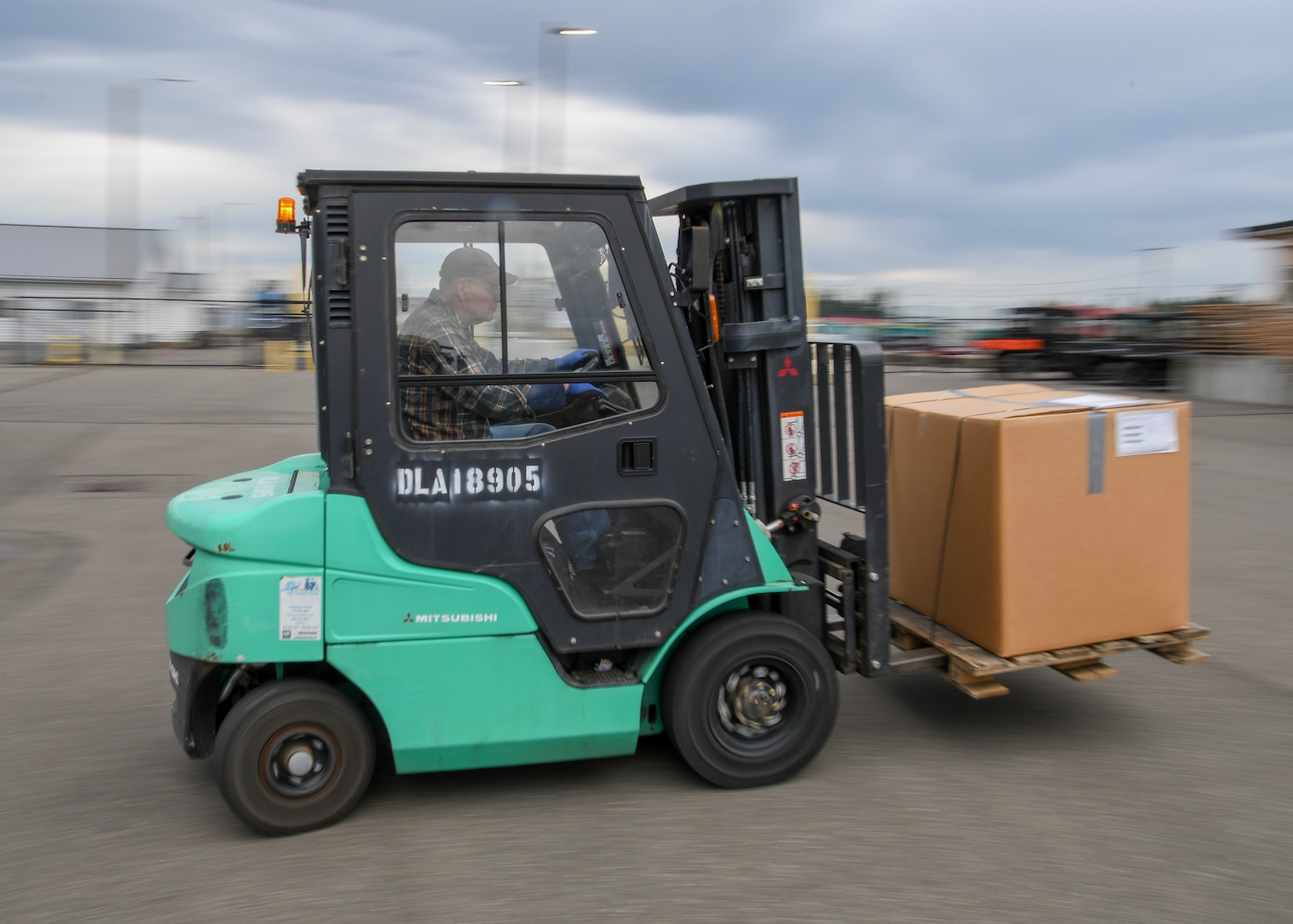 Green and Black Forklift moves cardboard boxes. the operation is taking place outside in what looks like a parking lot
