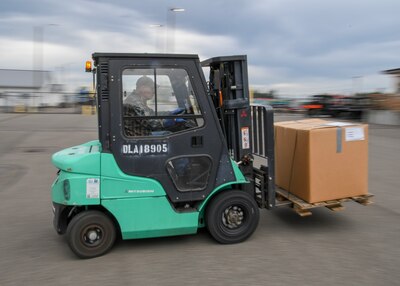 Green and Black Forklift moves cardboard boxes. the operation is taking place outside in what looks like a parking lot