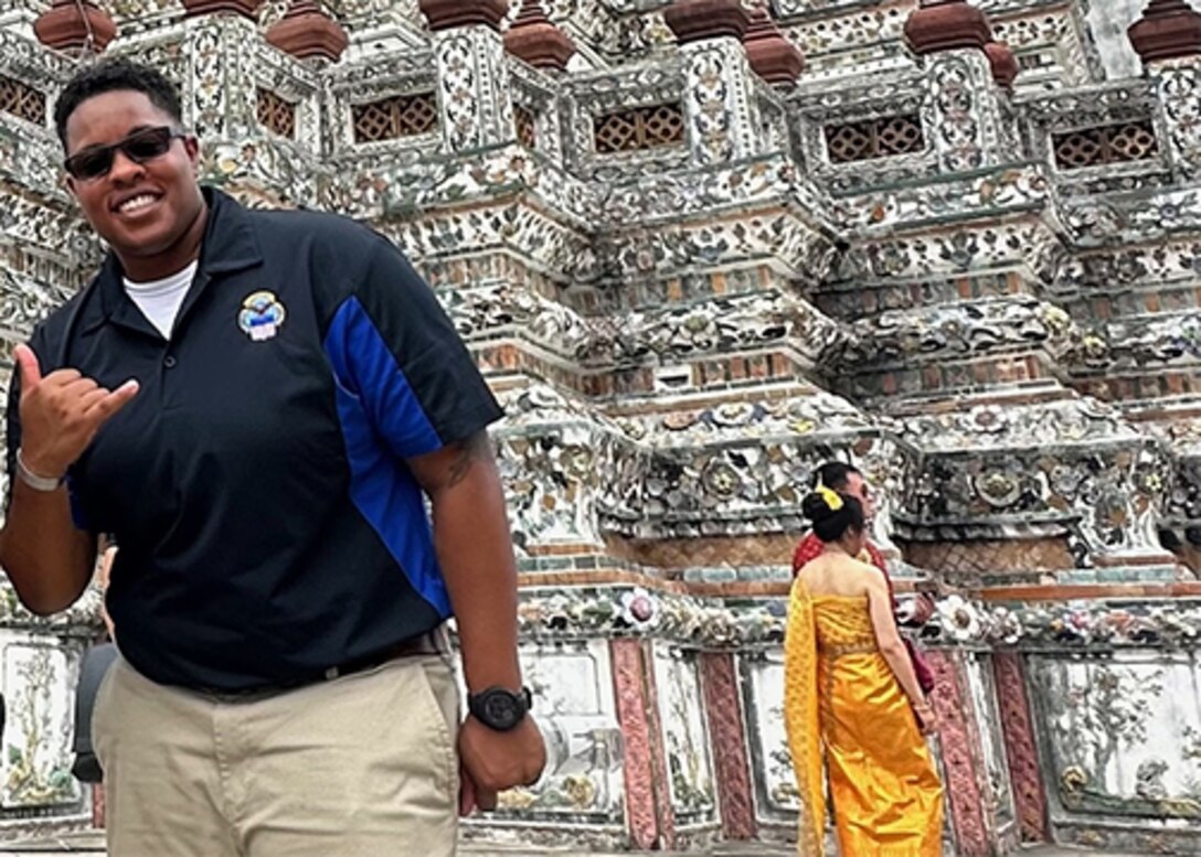 A Black woman in a dark shirt with a DLA logo poses for the camera with a traditional Thailand building behind her.
