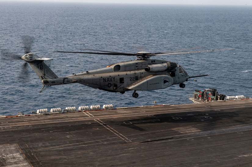 A helicopter hovers over an aircraft carrier at sea.