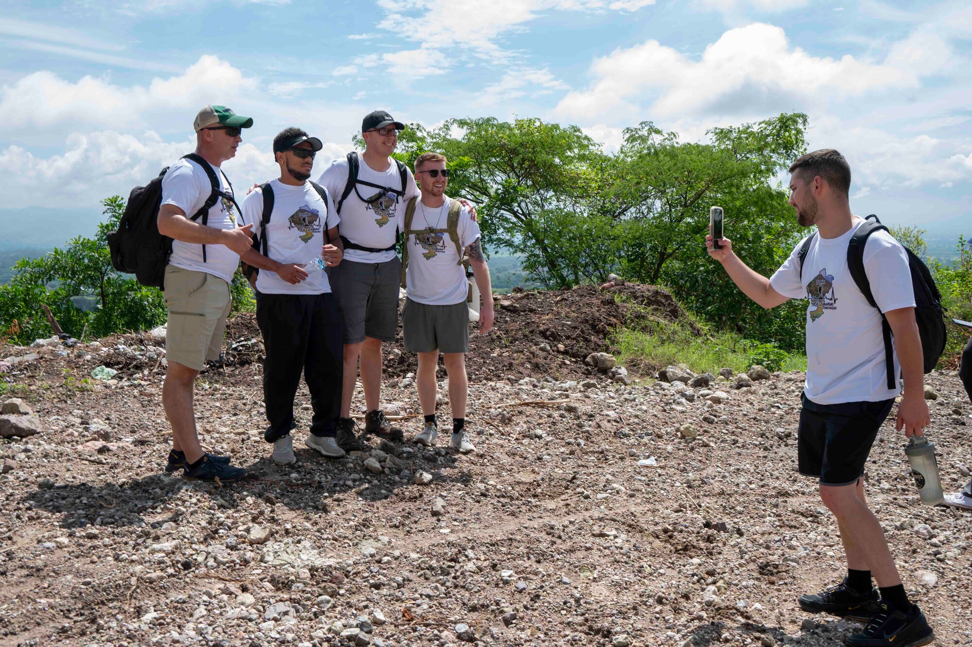 A group of four people pose for a photo while one person takes the picture on a phone.