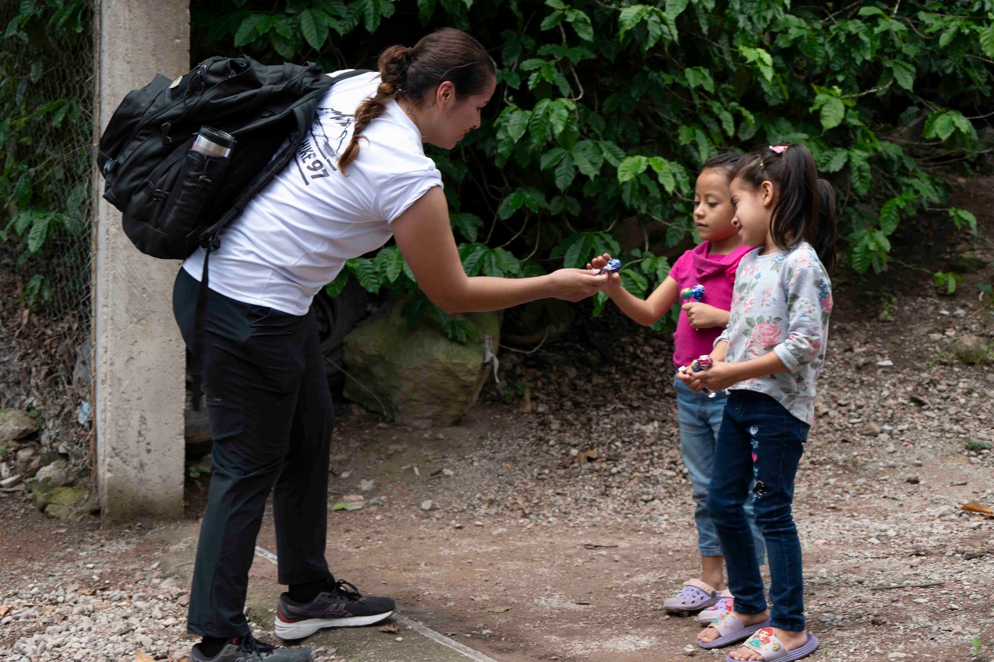 A person is bending down handing candy to two little girls.