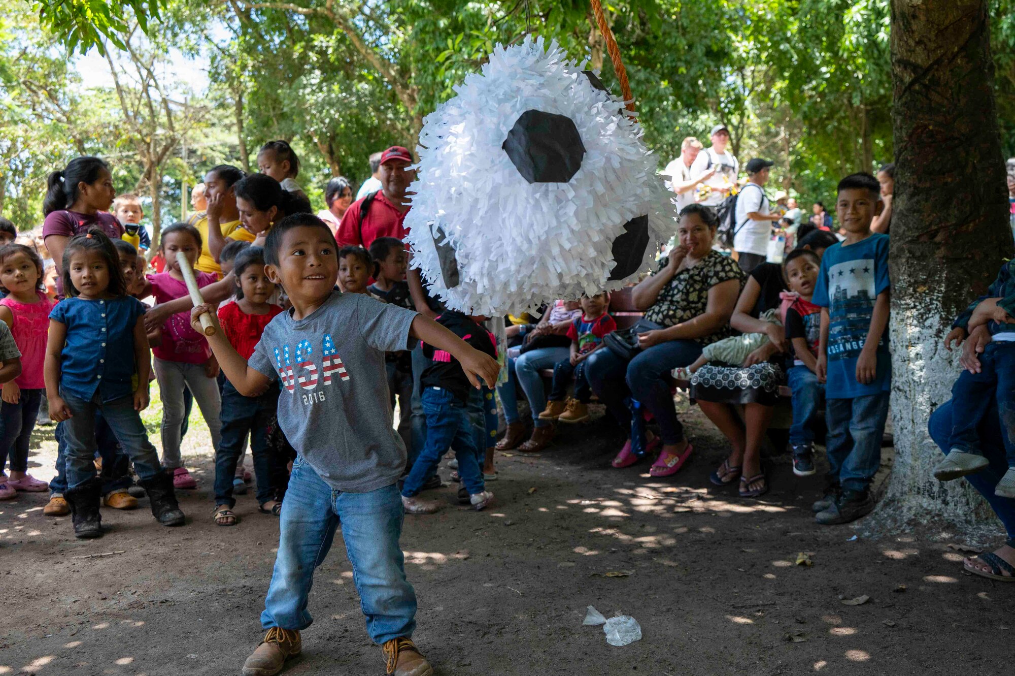 A kid swings a stick at a piñata while a crowd of other kids watch.