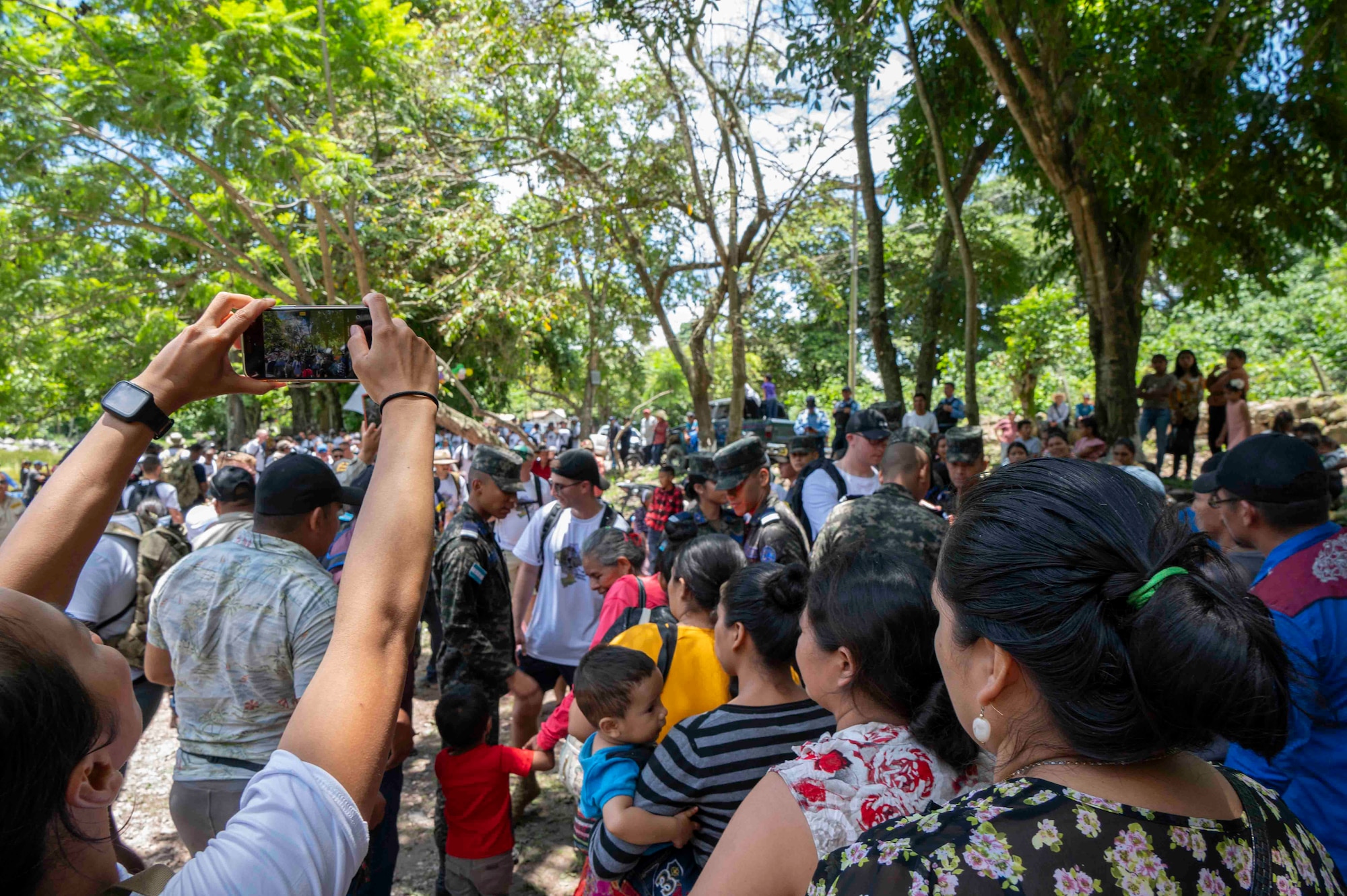 A photo of a crowd of people with one person taking a picture on their phone of everyone.