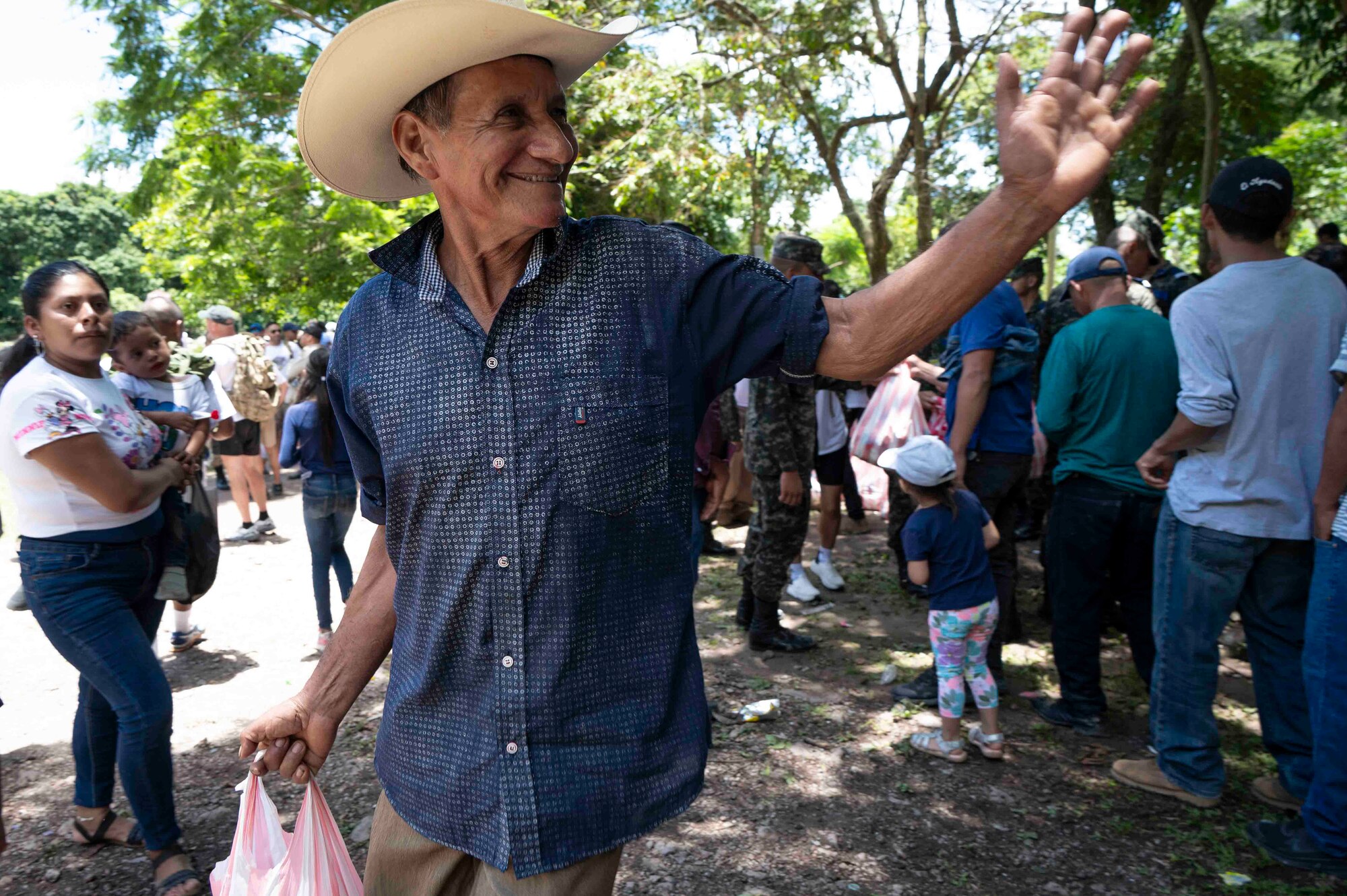A man in a cowboy hat smiles and waves while holding a bag of food.