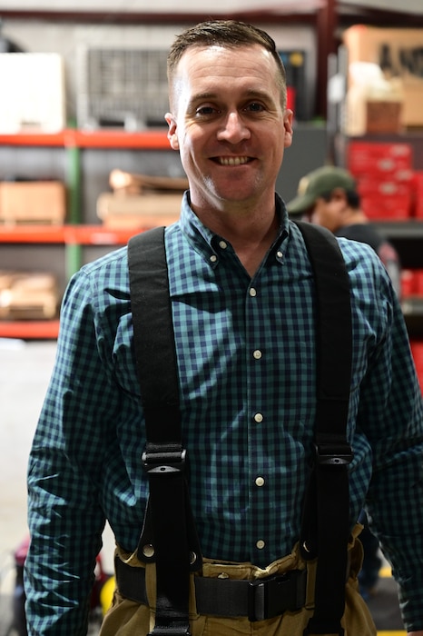 A man dressed in firefighter protective gear, standing and smiling.
