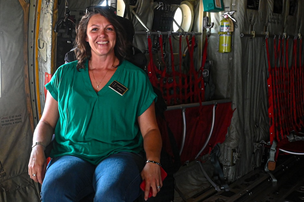 A woman is seated inside an Air Force cargo plane, smiling.