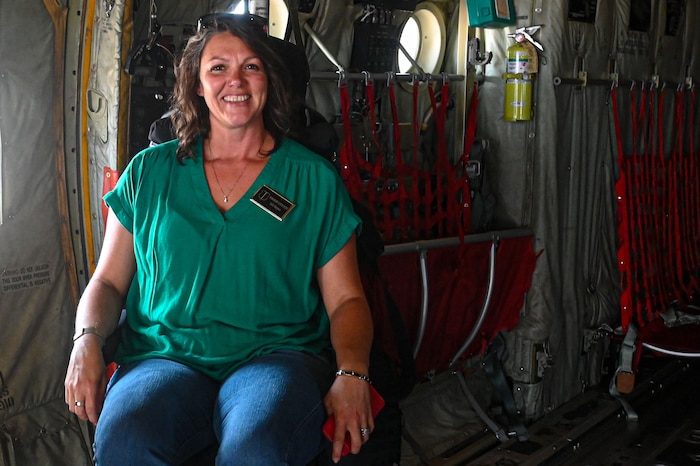 A woman is seated inside an Air Force cargo plane, smiling.