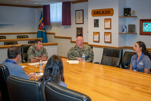 Two military officers and three teachers hold discussion at conference table.