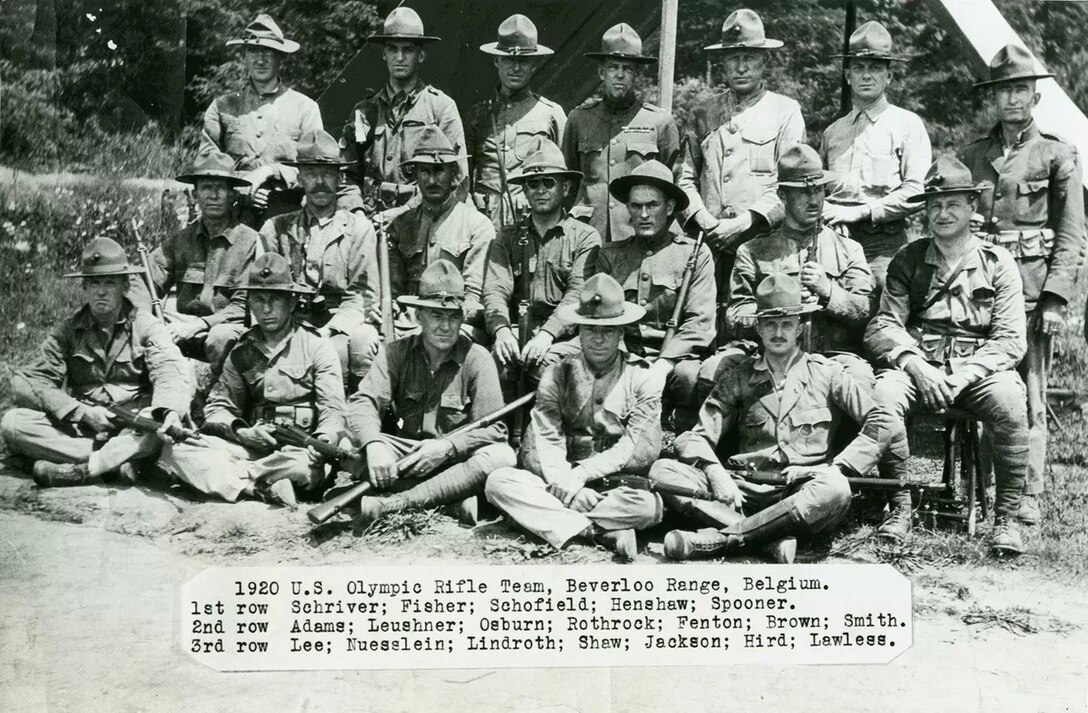 Three rows of men in khaki uniforms wearing brimmed hats. Some men are holding rifles.