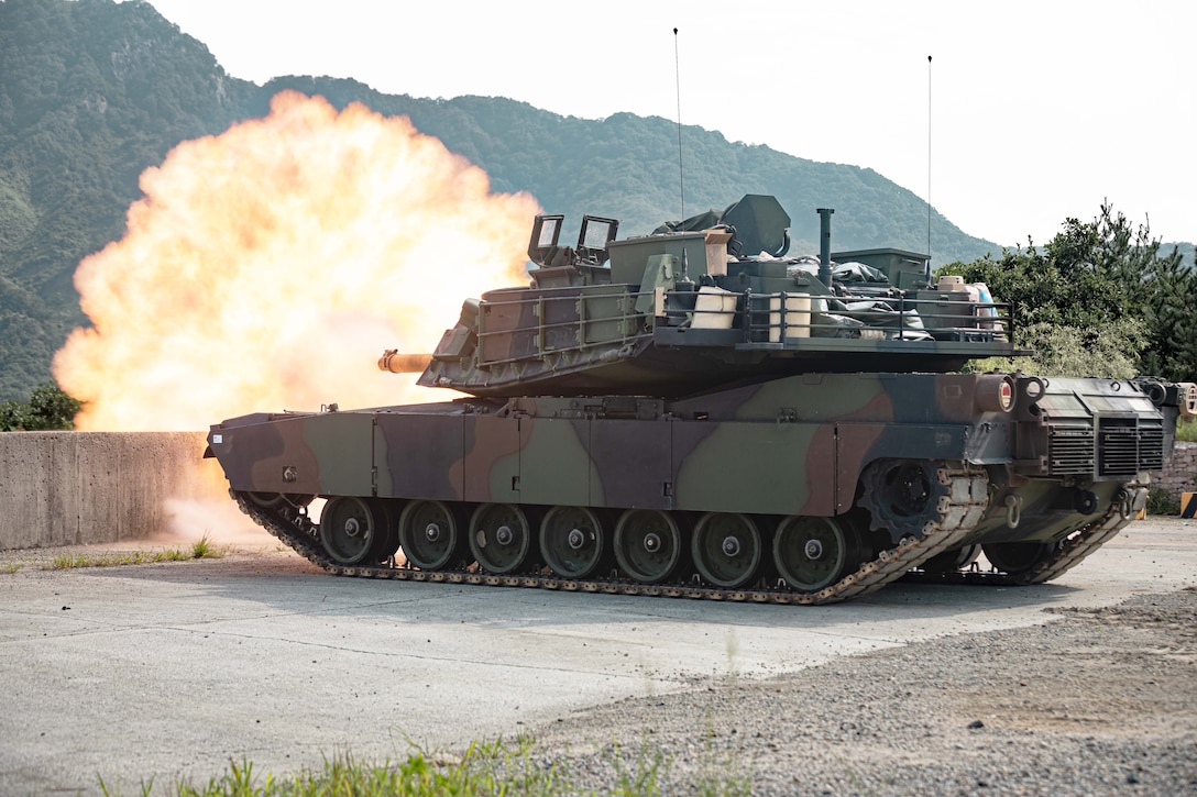 A tank fires creating a fireball towards mountains in the distance.