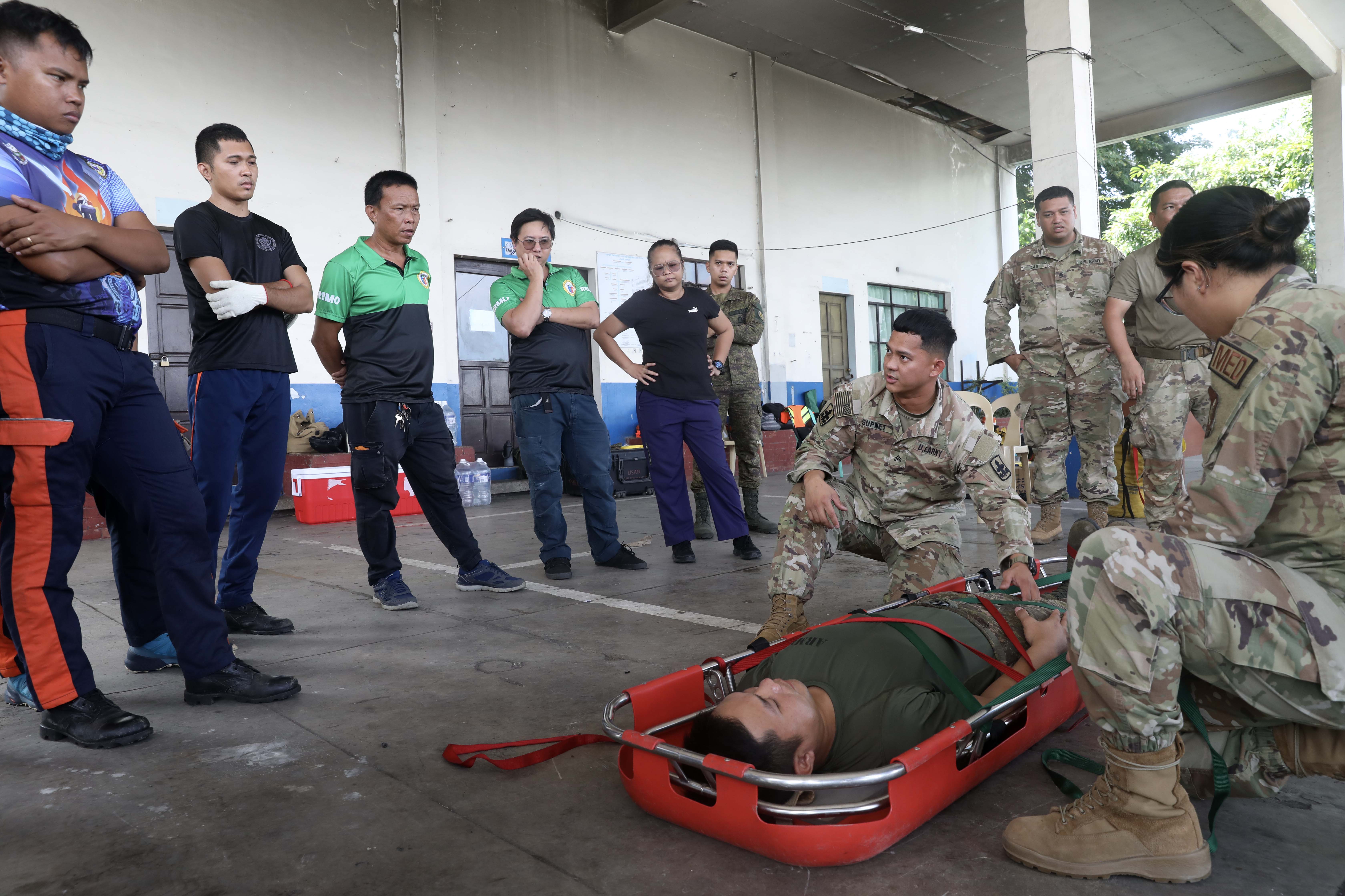 LEGAZPI, Philippines (Aug. 1, 2024) – Sgt. Conrad Supnet, left, of Whitmore, Hawaii, a member of the Hawaii Army National Guard and Tech. Sgt. Jane Cabusao of Kapolei, Hawaii, a member of the Hawaii Air National Guard, demonstrate patient packaging on Philippine Army Pfc. John Mark Quiroz of the 525th Combat Engineer Battalion in a stokes basket during an urban rescue training in support of the humanitarian aid and disaster response line of effort of Pacific Partnership 24-2 at the Legazpi airport in Legazpi, Philippines, Aug. 1, 2024. The training brought U.S. service members together with members of the 505th Search and Rescue Group, Philippine Air Force, the 525th Combat Engineer Battalion of Combat Engineer Regiment of the Philippine Army, Legazpi City officials, the Disaster Risk Reduction and Management Office and members of the Bureau of Fire Protection, to share ideas and experiences allowing them to teach and learn from one another. Now in its 20th iteration, the Pacific Partnership series is the largest annual multinational humanitarian assistance and disaster relief preparedness mission conducted in the Indo-Pacific. Pacific Partnership works collaboratively with host and partner nations to enhance regional interoperability and disaster response capabilities, increase security and stability in the region, and foster new and enduring friendships in the Indo-Pacific. (U.S. Navy photo by Mass Communication Specialist 1st Class Ryan D. McLearnon/Released)