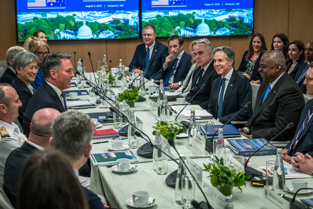 A group of government and military leaders sit around and talk at a large conference table.