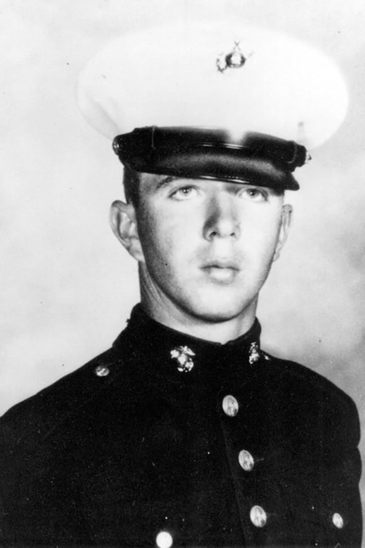 A service member in uniform and cap poses for a black and white photo.