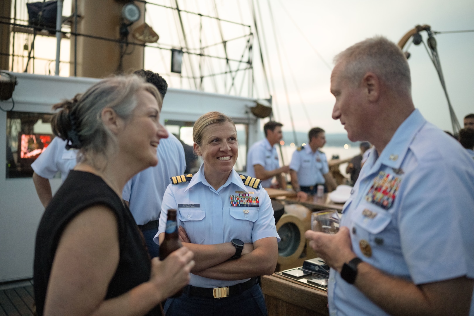 U.S. Coast Guard Cmdr. Megan Drewniak, deputy commander of Sector Northern New England, middle, speaks with Master Chief Petty Officer Rob Riemer, Sector Northern New England command master chief, at U.S. Coast Guard Cutter Eagle’s reception to honor Rockland, Maine, as an official Coast Guard City, in Rockland, Maine, Aug. 3, 2024. Rockland recertified to become a Coast Guard City, demonstrating a mutually beneficial relationship between the local Coast Guard community and the City of Rockland.