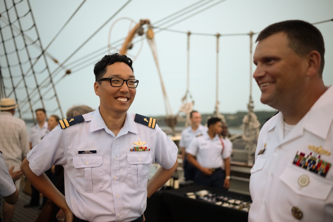 U.S. Coast Guard Academy Chaplain Lt. Paul Song shares a laugh with U.S. Navy Cmdr. Jeremy Chase, the commanding officer of the USS Delbert D. Black (DDG 119), aboard Coast Guard Cutter Eagle (WIX 327), during a reception to celebrate Rockland, Maine, as a Coast Guard City, Aug. 2, 2024. Eagle’s command, crew and Coast Guard Academy cadets hosted the reception while the ship was anchored in Rockland Harbor near the Delbert Black.