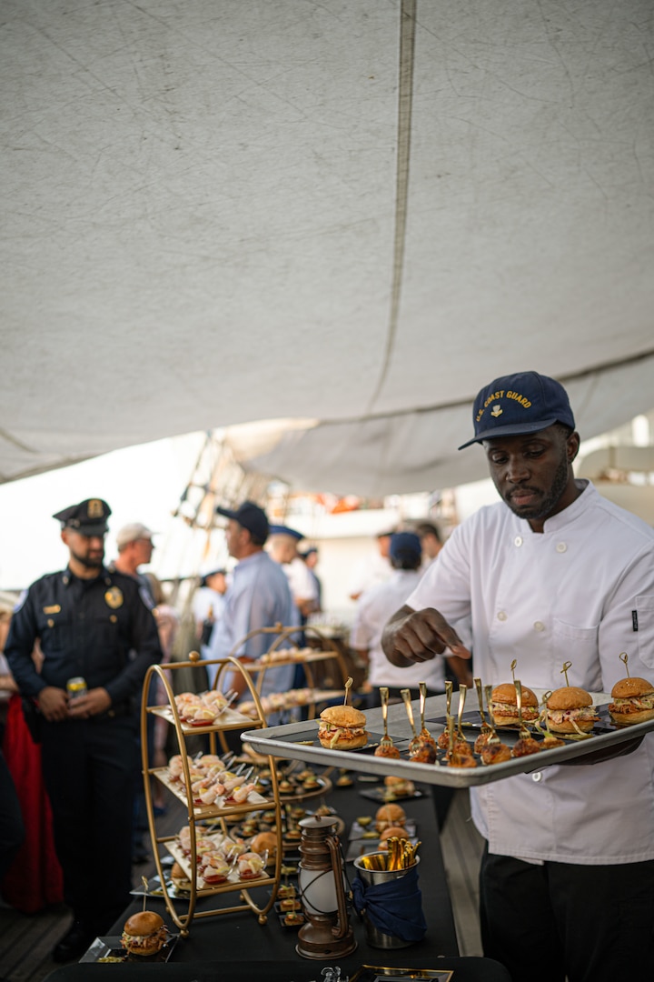 U.S. Coast Guard Petty Officer 2nd Class Kenlee Mars, a culinary specialist assigned to Coast Guard Cutter Eagle (WIX 327), places prepared dishes on a table for a reception to celebrate Rockland, Maine, as a Coast Guard City, Aug. 2, 2024. Eagle’s command, crew and Coast Guard Academy cadets hosted the reception while the ship was anchored in Rockland Harbor.