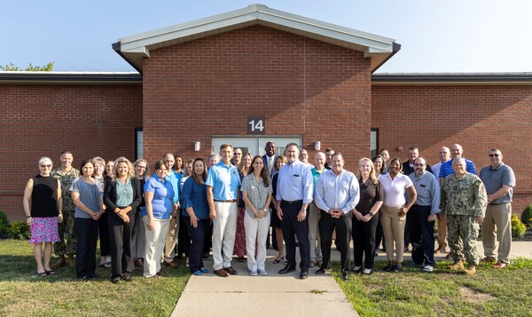 Group of people pose for photo in front of brick building