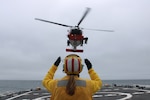 Ensign Matalynn Clark, a U.S. Coast Guard Cutter Kimball (WMSL 756) crew member, relays landing signals to an MH-60 Jayhawk helicopter aircrew from USCG Air Station Kodiak during a helicopter landing evolution while Kimball patrols the Bering Sea, May 11, 2024. During their patrol, Kimball also operated with a forward deployed MH-60 Jayhawk helicopter and aircrew in Cold Bay, Alaska, and the District Seventeen command center to execute complex SAR exercises for improving, coordination, response times, and range of rotary Coast Guard assets to assist mariners in distress. U.S. Coast Guard photo by Ensign James Bongard.