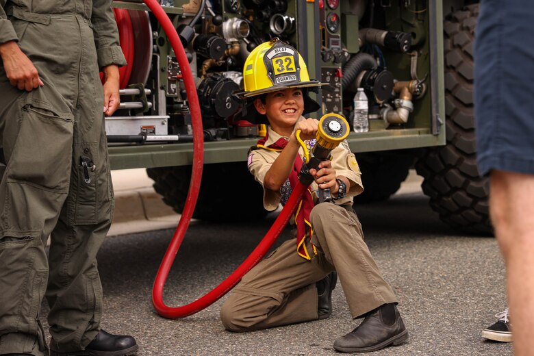 A child with Boy Scouts of America pretends to spray a firehouse during the National Night Out at the Crossroads Elementary School on Marine Corps Base Quantico, Virginia, August 6, 2024. The purpose of National Night Out is to enhance the relationships between law enforcement and the people they protect. (U.S. Marine Corps photo by Lance Cpl. David Brandes)