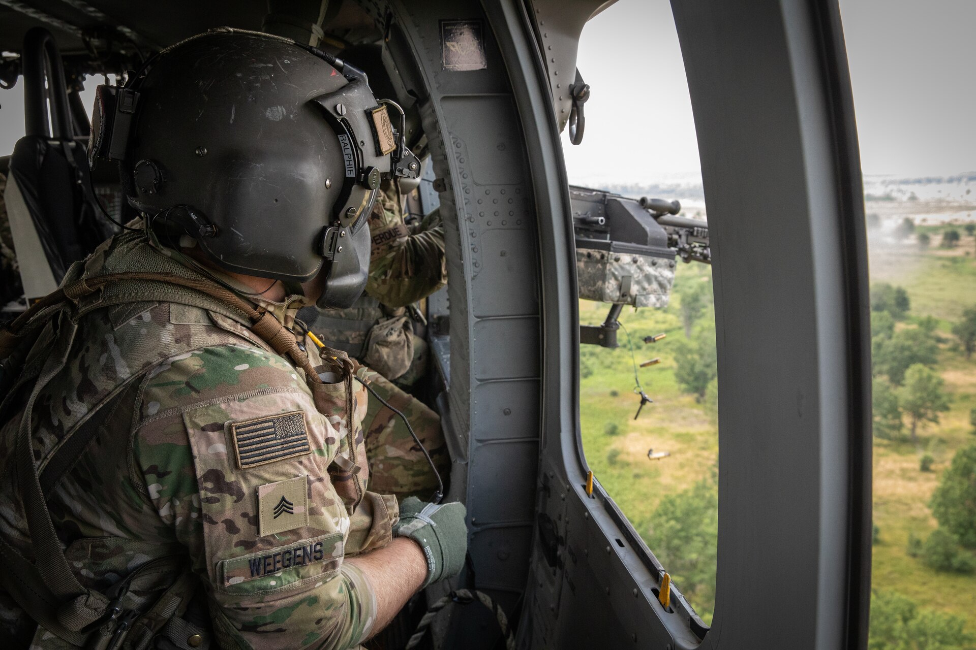 U.S. Army Sgt. Michael Weegans gives instruction to Sgt. Noah Perdue during gunnery in a UH-60 Blackhawk at Camp Grayling Army Airfield in Grayling, Michigan on July 16, 2024. Weegans and Perdue are a Soldiers in Bravo Company 2/147th Assault Helicopter Battalion, 63rd Theater Aviation Brigade,  who was conducting aerial gunnery during their annual training. (U.S. Army National Guard photo by Sgt. 1st Class Andrew Dickson)