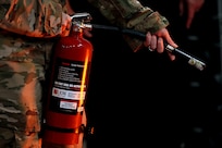 Airman holding a fire extinguisher pointing nozzle to the right.