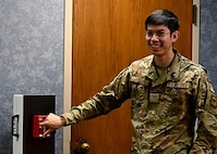 Airman demonstrates activating fire alarm in a hallway.