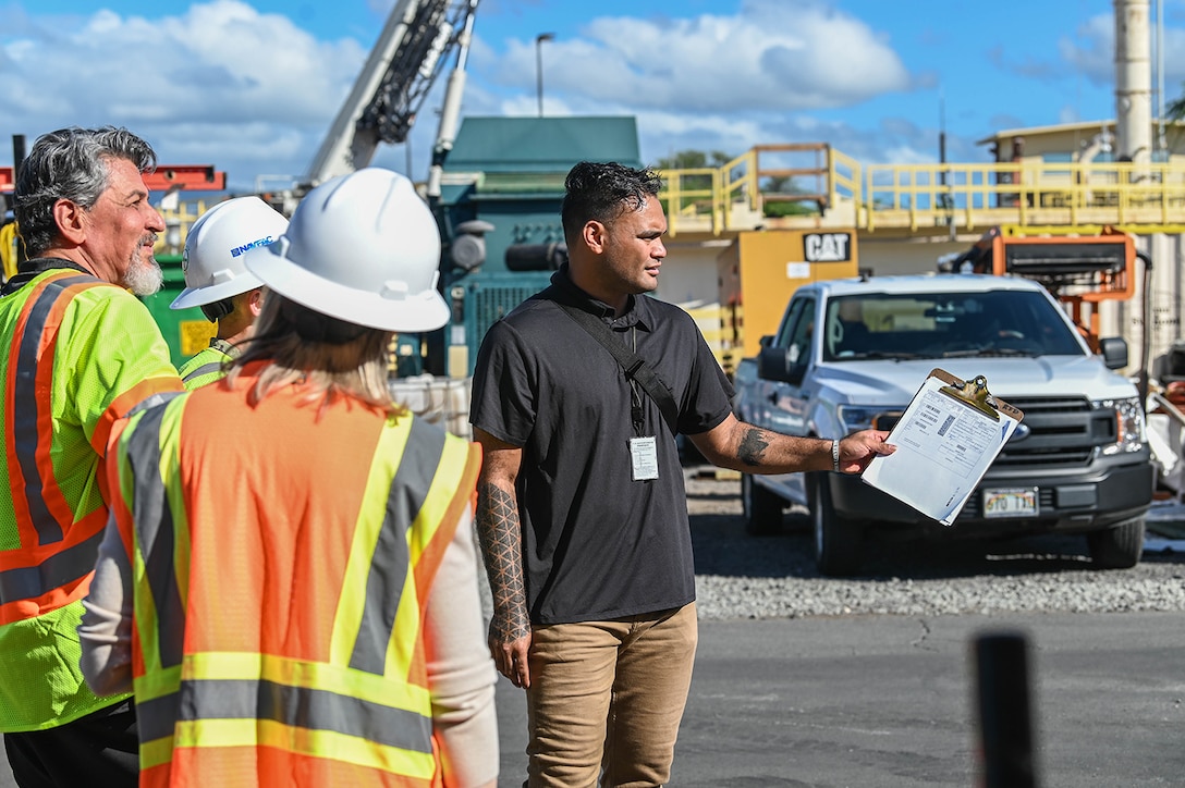 A man talks with others in an industrial outdoor setting.