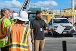 A man talks with others in an industrial outdoor setting.
