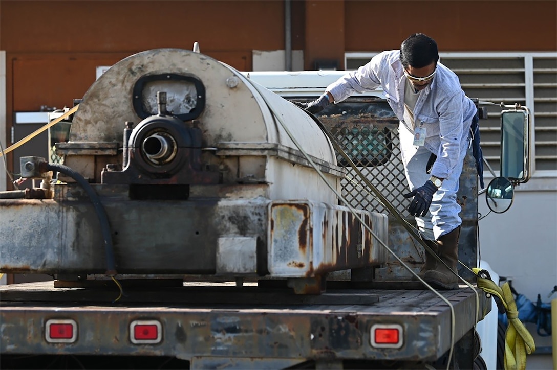 A man secures a large piece of equipment on a flatbed truck.