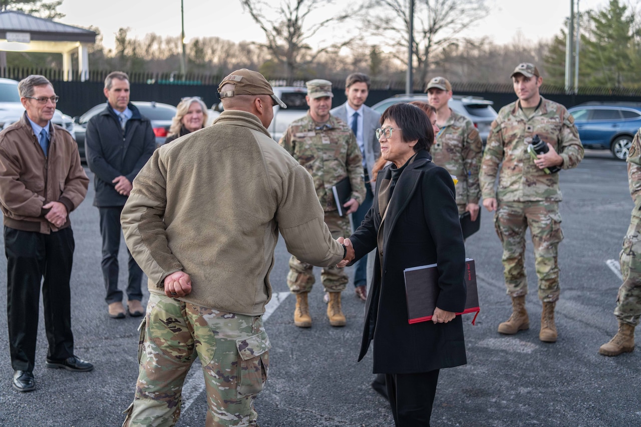 A woman in civilian attire shakes hands with a service member in uniform.